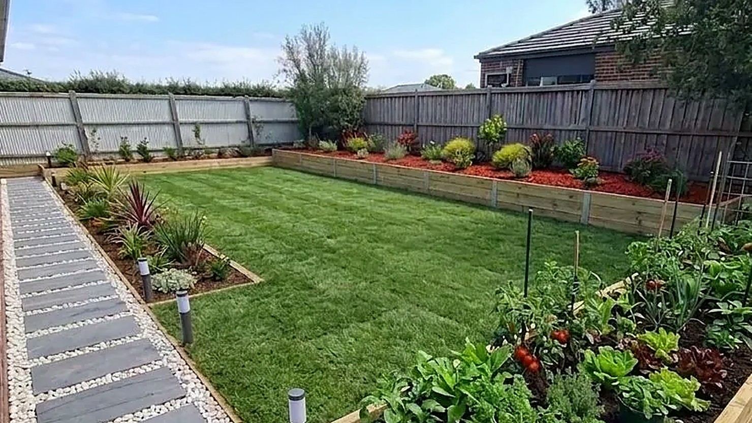 Backyard garden with planted borders, raised veg beds and stepping-stone path by Bastiano Landscaping