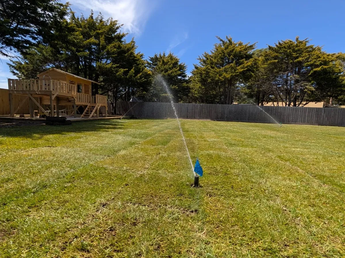 Sprinkler watering an established lawn beside a timber deck and treeline
