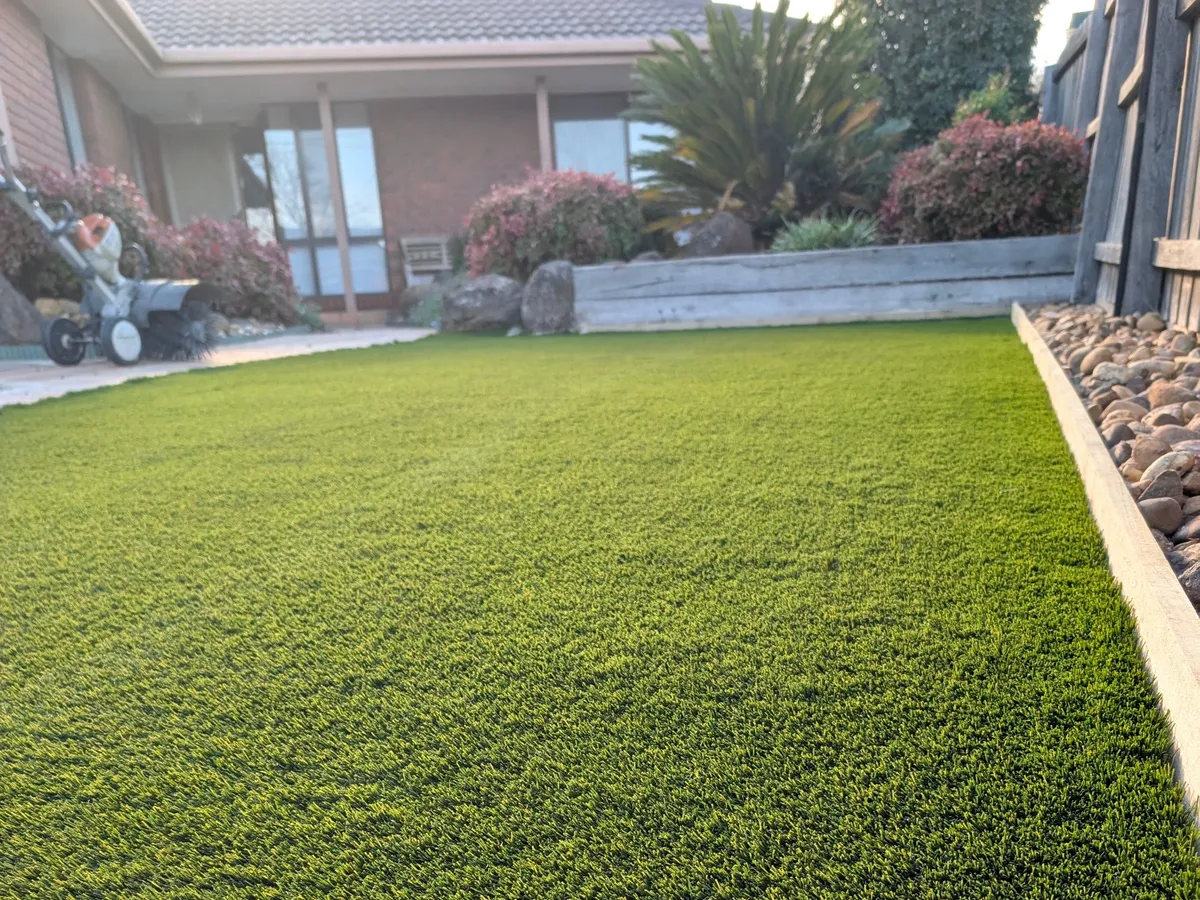 Synthetic front lawn with a river-pebble border, freshly power-brushed