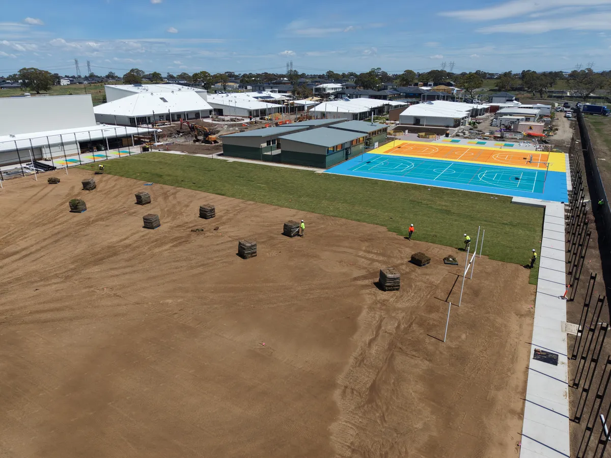 Aerial view of natural turf being laid across a school sports field beside new multi-sport courts