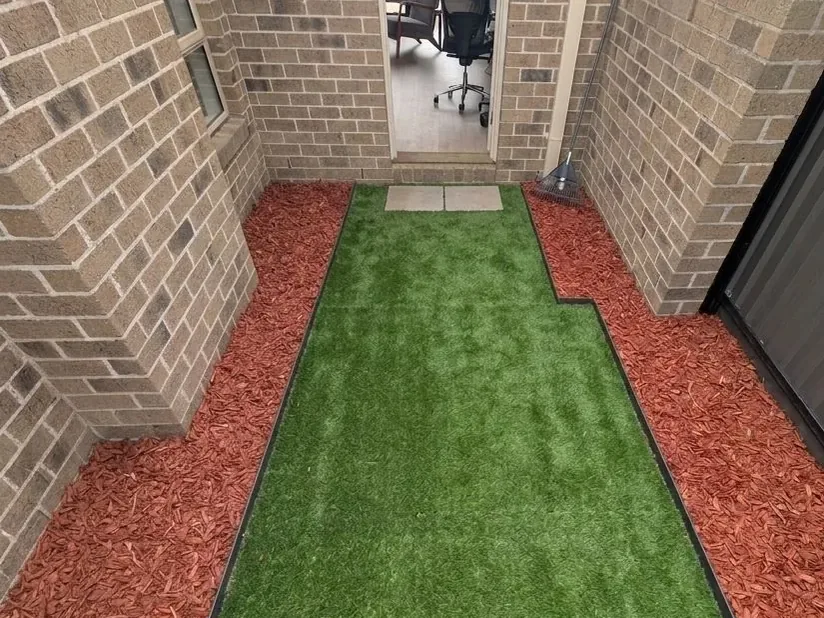 Synthetic turf with red mulch borders in a narrow brick courtyard