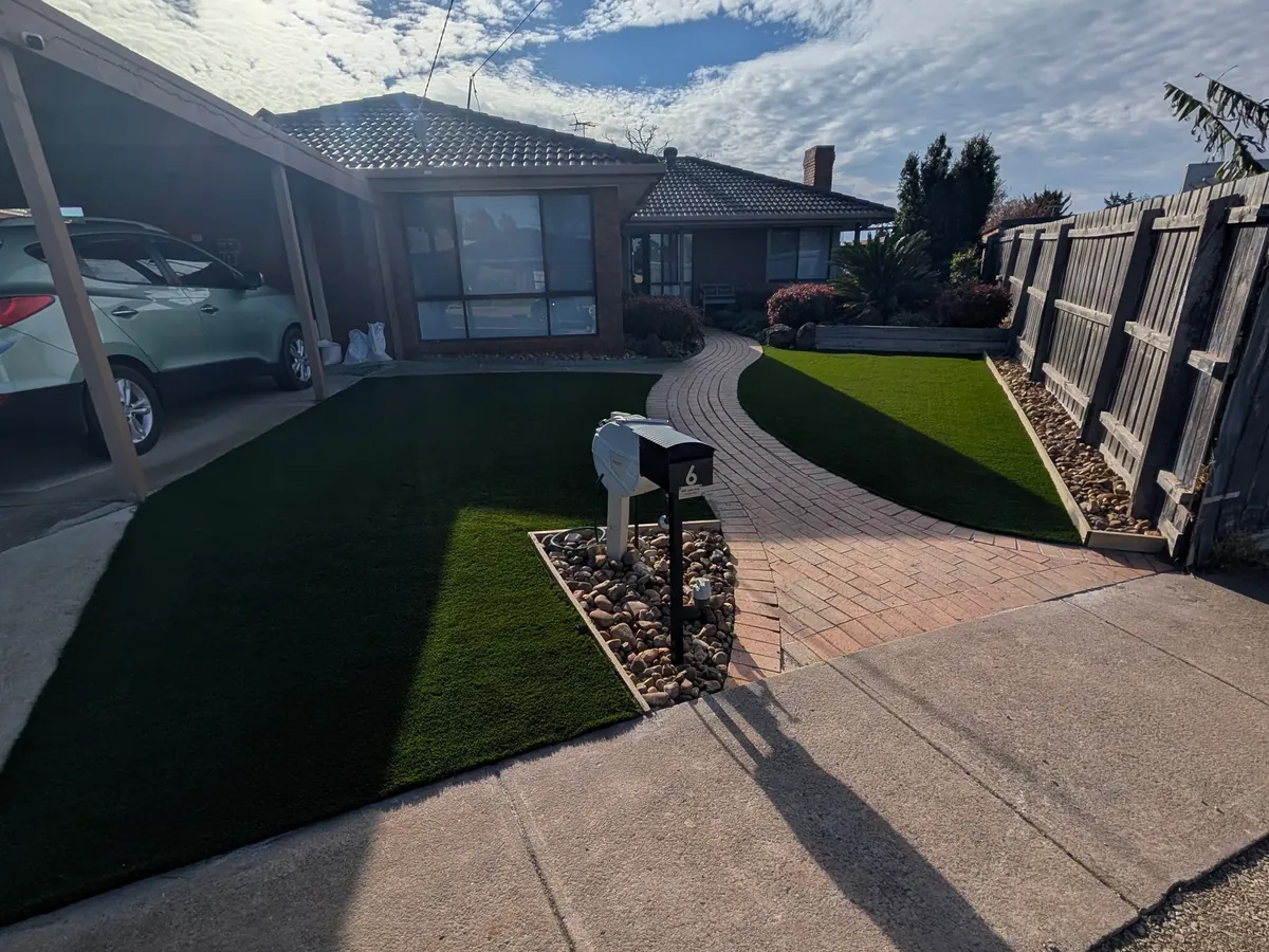 Curved synthetic front lawn beside a brick path and driveway