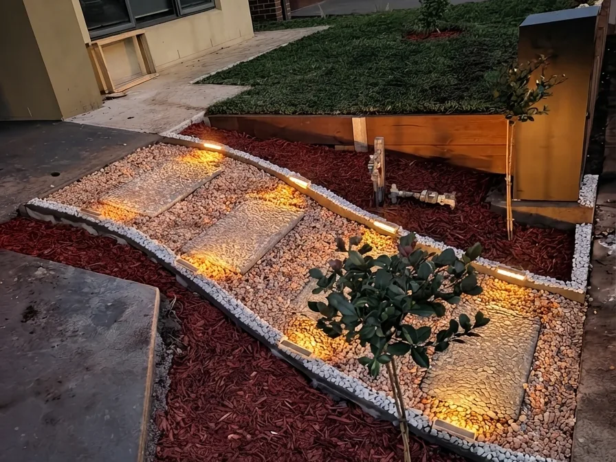 After: raised lawn edge, illuminated stepping stones, white-pebble detailing, red mulch and feature planting