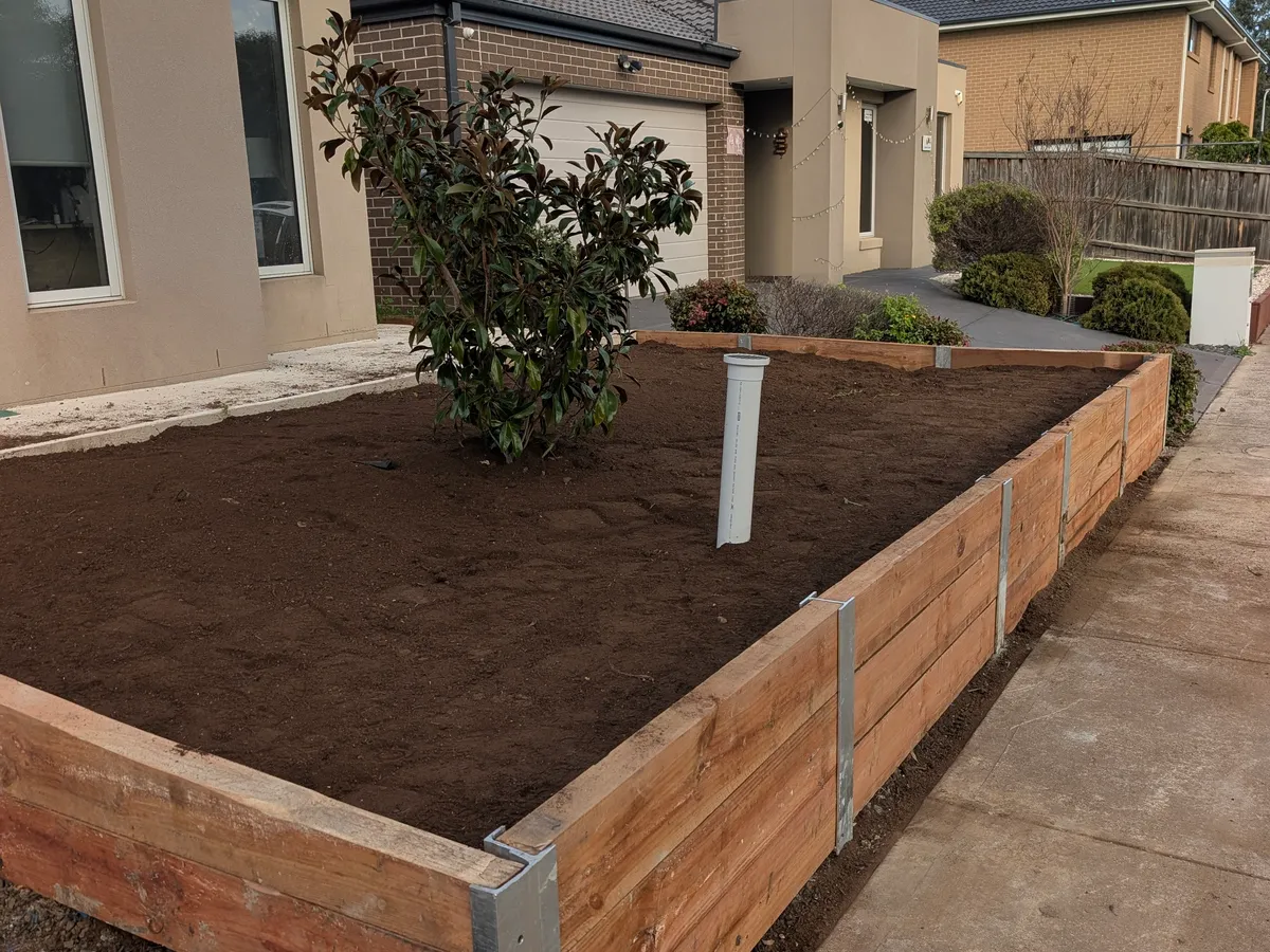 Treated-pine planter wall under construction with fresh topsoil