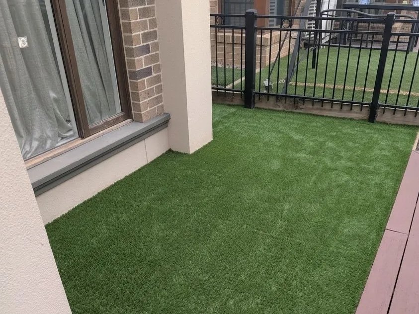 Synthetic turf laid wall-to-wall across a courtyard beside a merbau deck and black balcony railing